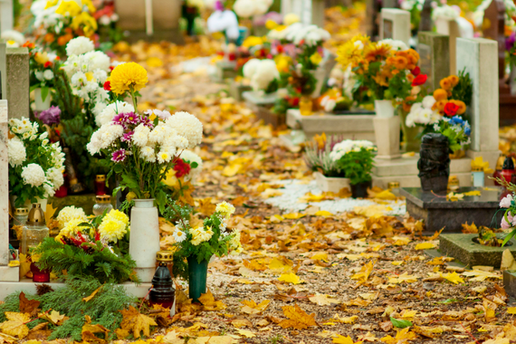 Cmentarz jesienią, groby przyozdobione kwiatami i zniczami, żółte liście na ziemi